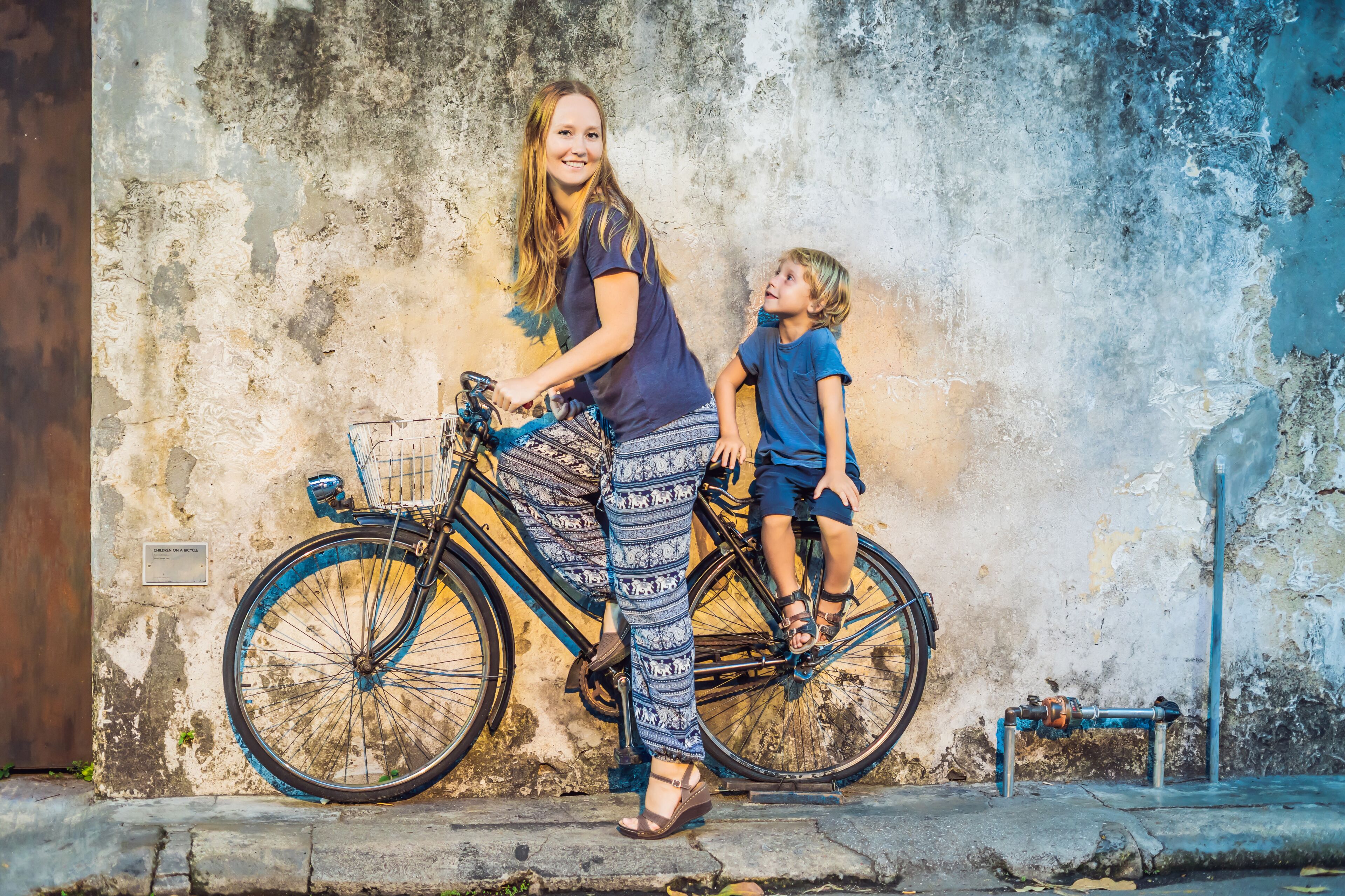 Una mujer y un niño en bicicleta frente a una pared con textura.