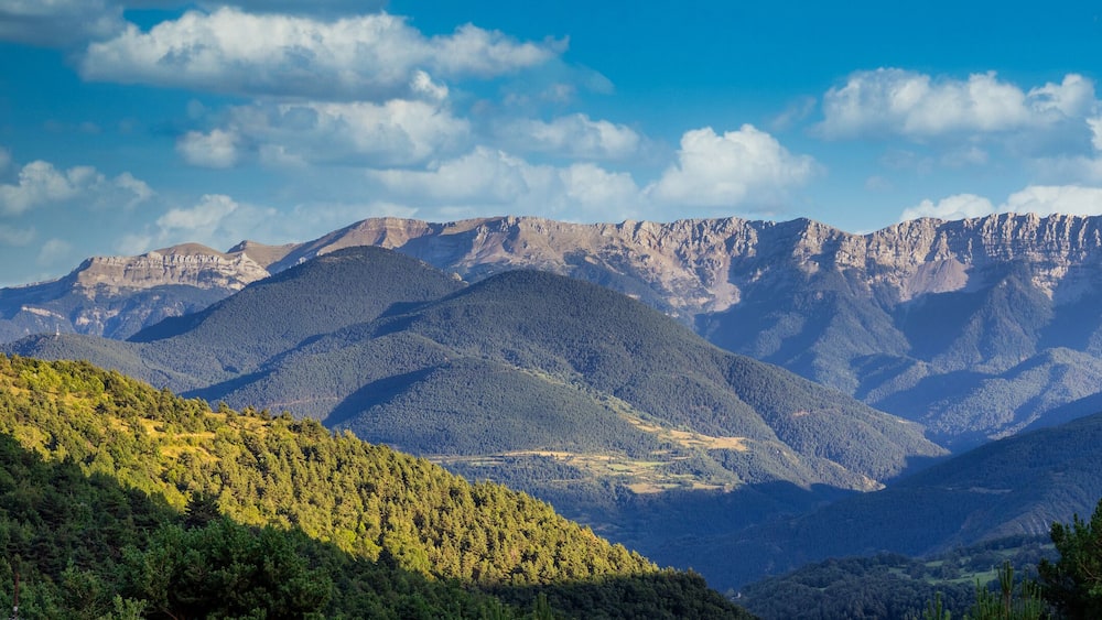 A mountain range with dense forests and rugged peaks under a clear sky.