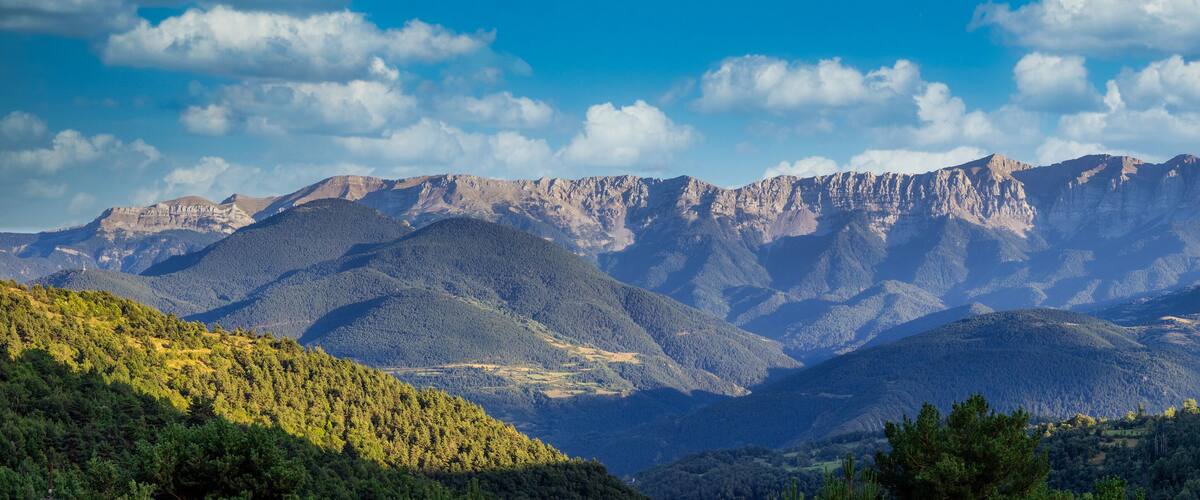 A mountain range with dense forests and rugged peaks under a clear sky.