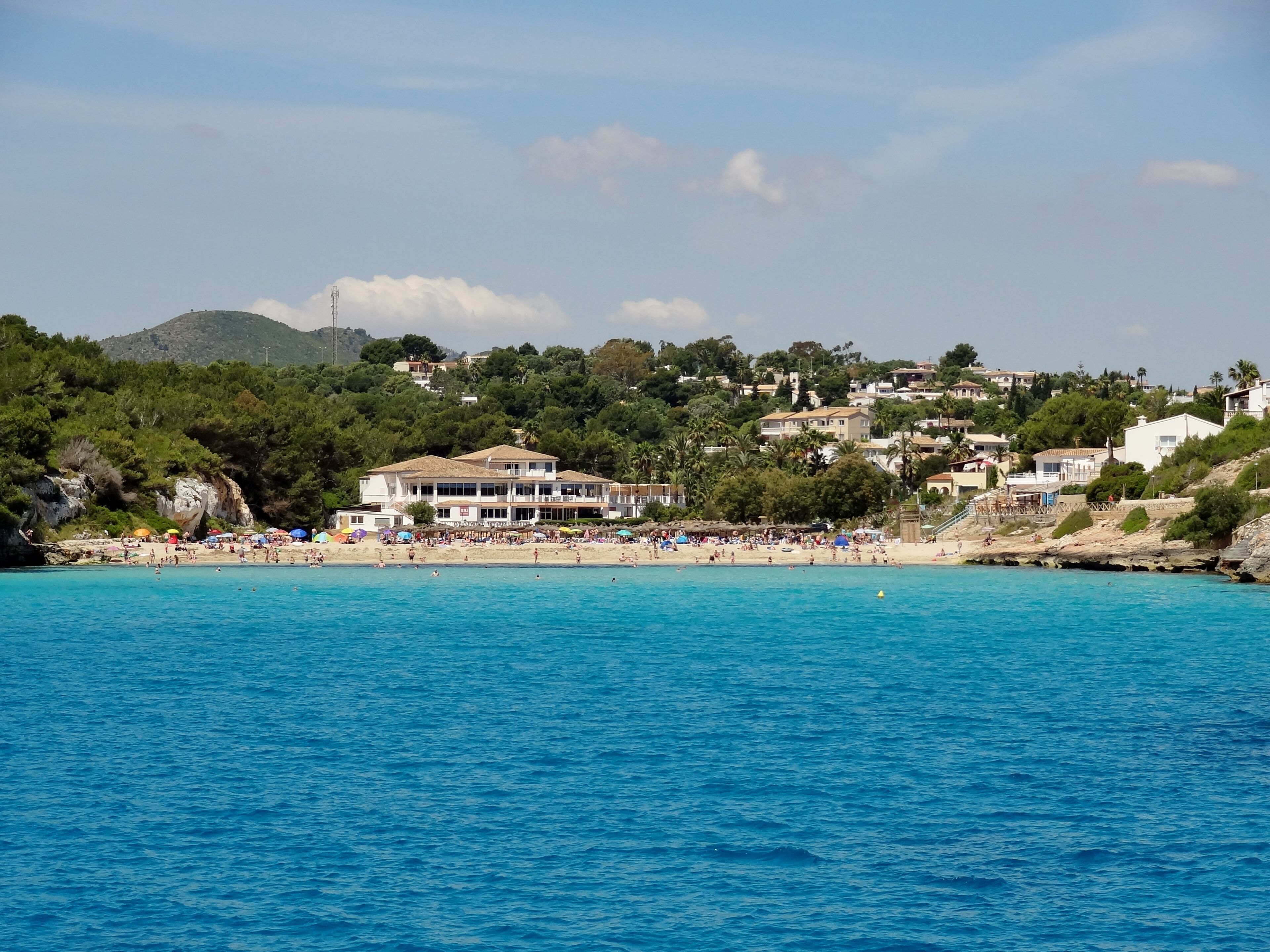 A coastal town with a beach, clear blue waters, and buildings on a hillside.