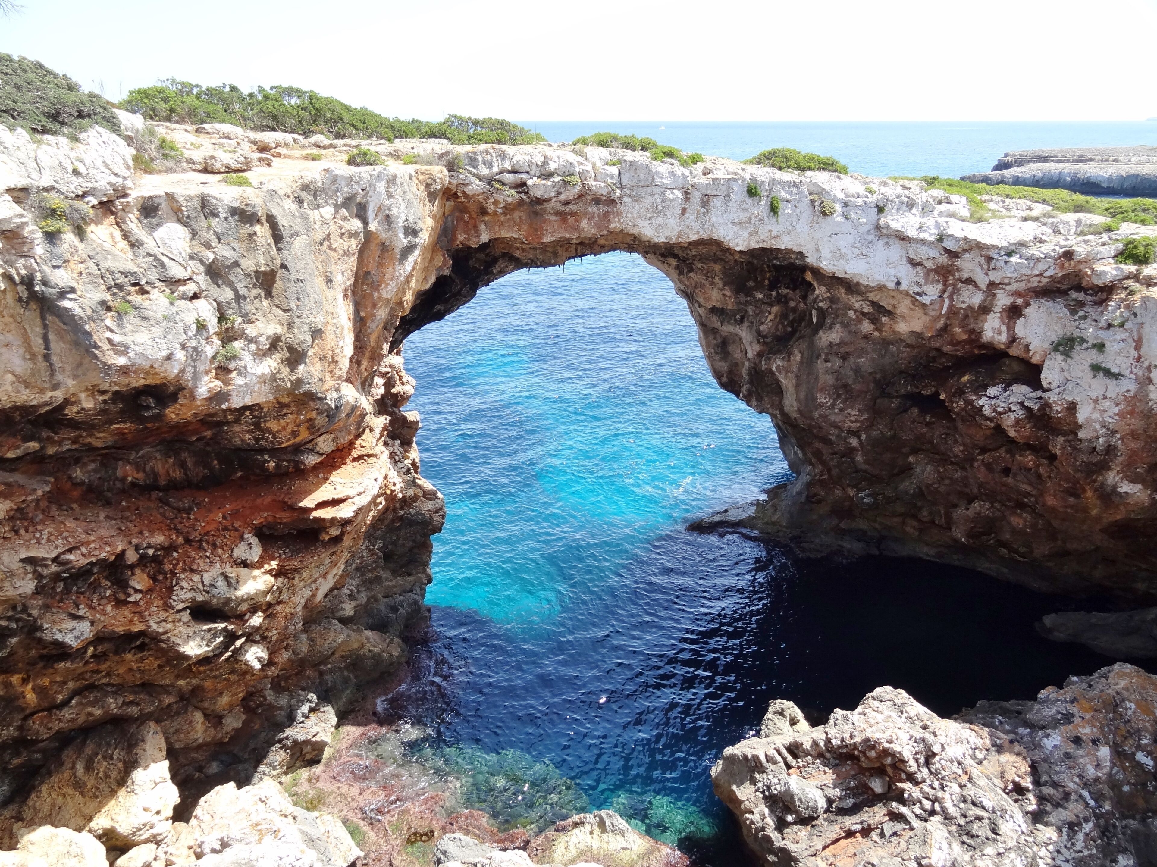 A natural rock arch over a clear blue sea.