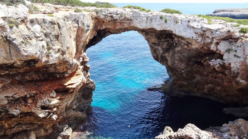 A natural rock arch over a clear blue sea.