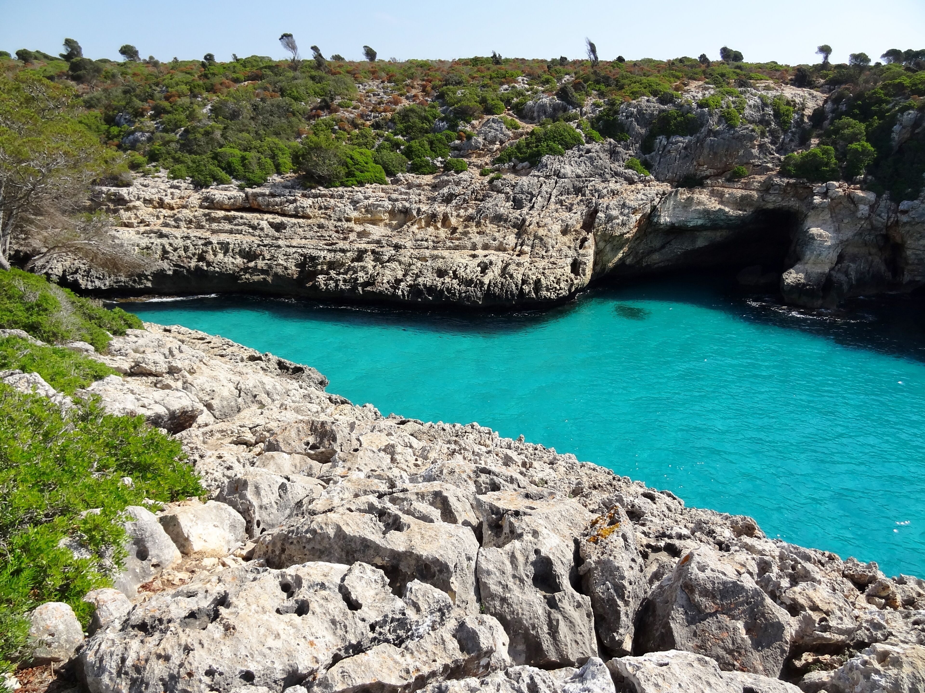 A rocky coastline with a turquoise sea, cliffs, and sparse vegetation.