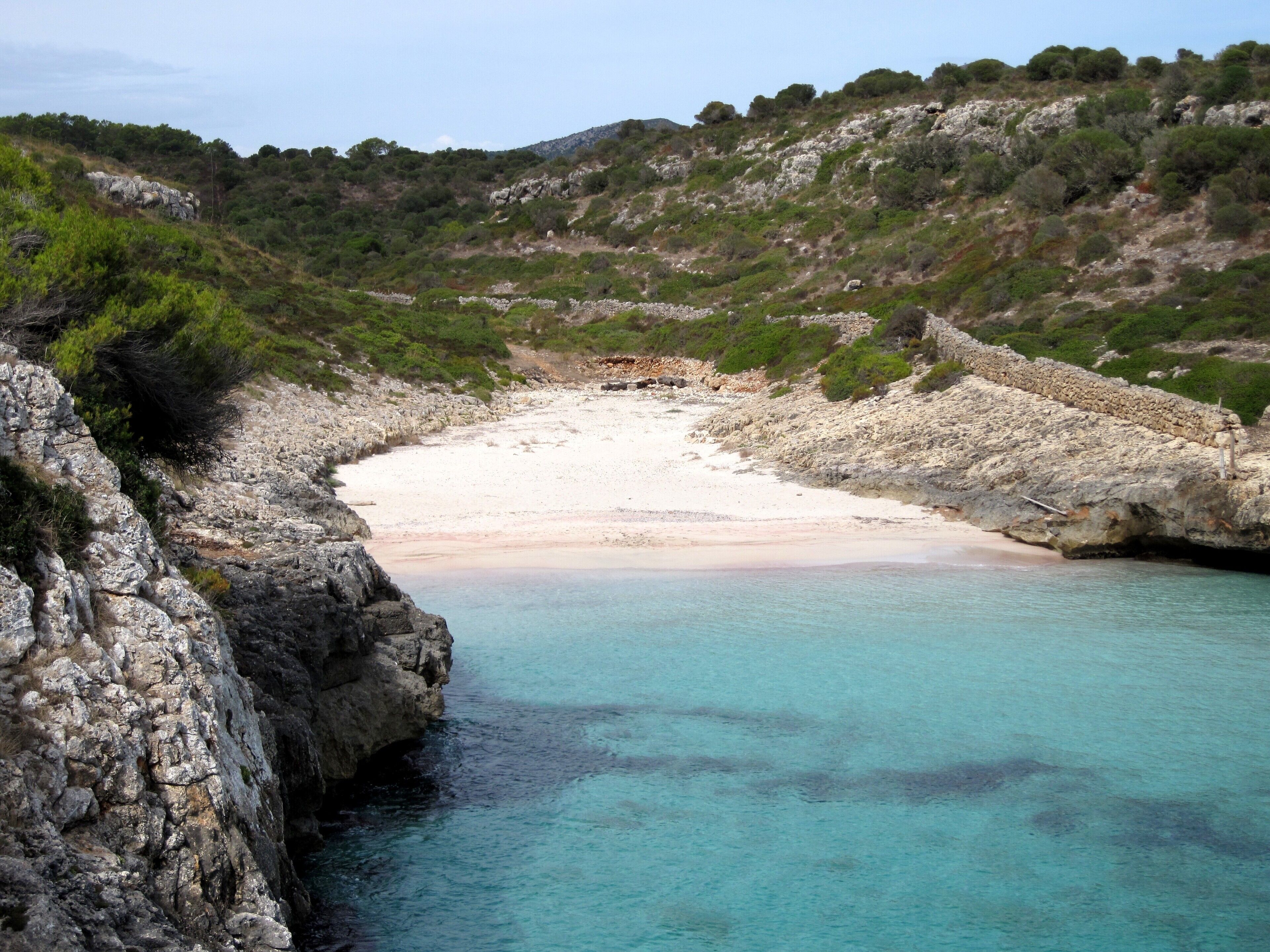 A coastal landscape with a rocky shoreline, clear turquoise water, and a sandy beach.