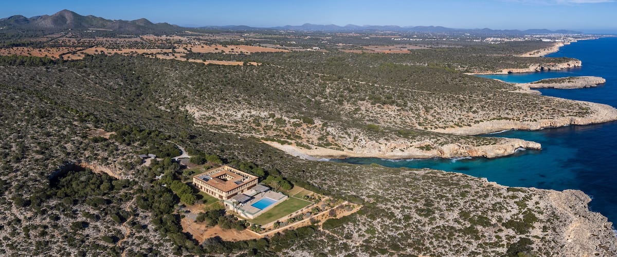 A coastal landscape with rocky cliffs, a beach, and a large building with a swimming pool.