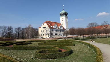A historic building with a tower and a well-maintained garden with geometric hedges.