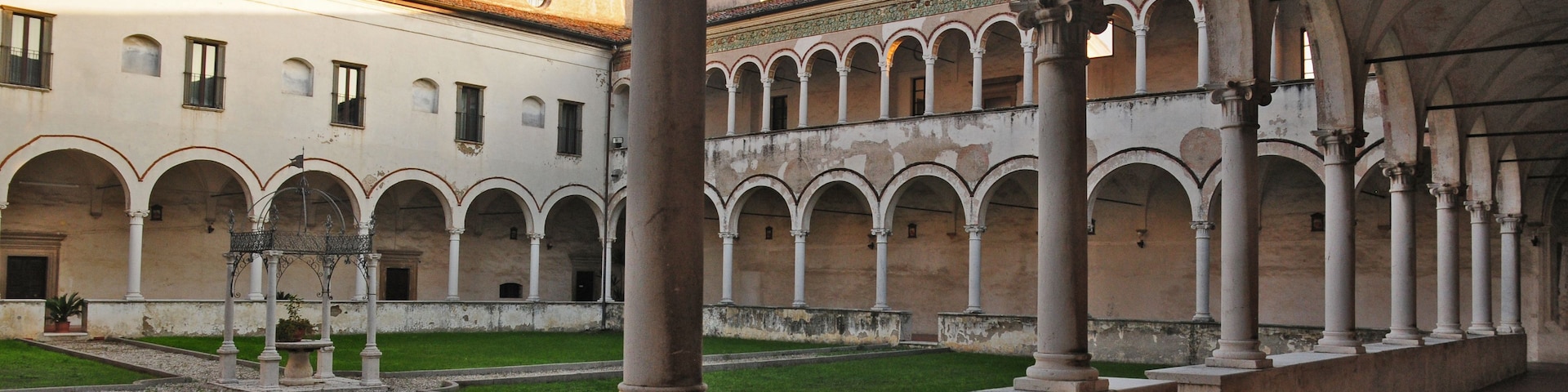 Un claustro antiguo con un patio central, rodeado de galerías con arcos y columnas.