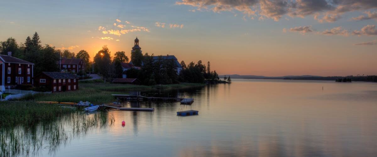 A calm lake at sunset with boats, a church, and houses along the shore.