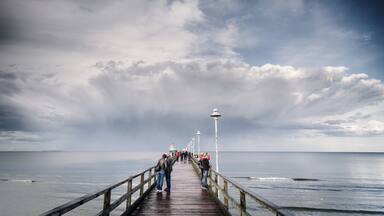 A wooden pier extending into the sea with people walking along it.