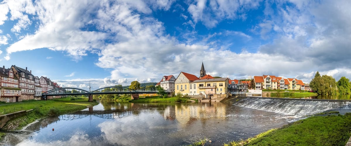 A river with a bridge, traditional half-timbered houses, and a church with a spire.