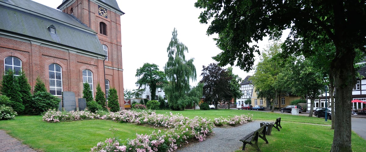 A brick building with a clock tower, a paved path, and flower beds.