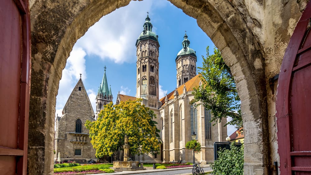 Ein Bogen, der eine historische Kirche mit zwei TĂŒrmen und einen Baum im Vordergrund umfasst.
