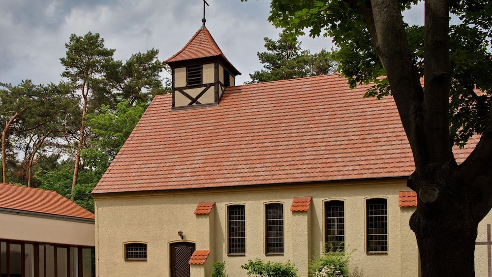 Eine Kirche mit rotem Ziegeldach, einem Glockenturm und einem Kreuz auf der Spitze.