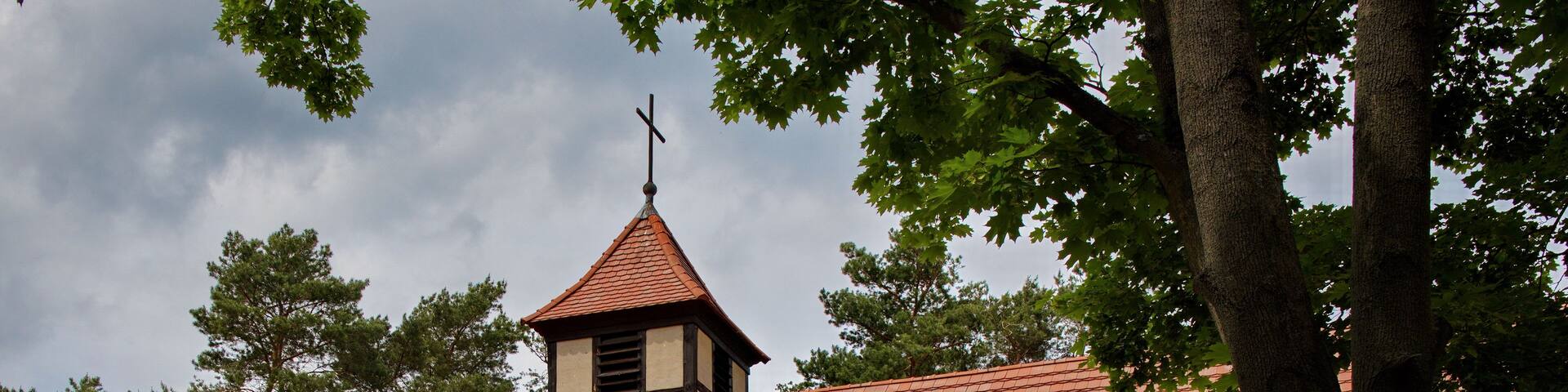 A church with a red-tiled roof, a bell tower, and a cross on top.