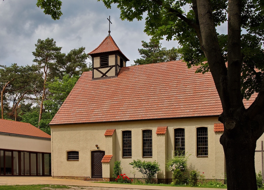 Une église avec un toit recouvert de tuiles rouges, un clocher et une croix au sommet.