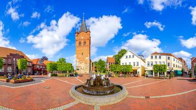 A town square with a prominent tower, a fountain, and historic buildings.