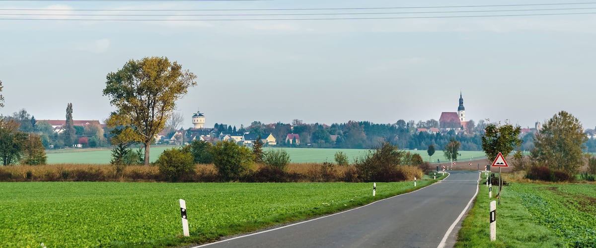 A rural road with fields, a water tower, and a distant town with a church tower.