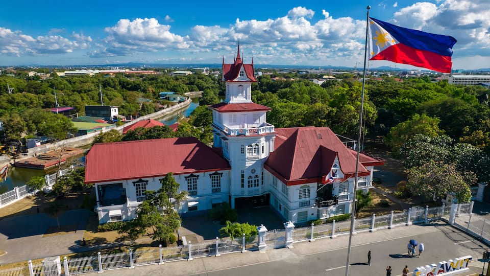 A white building with a red roof, a tower, and a flagpole with a flag.