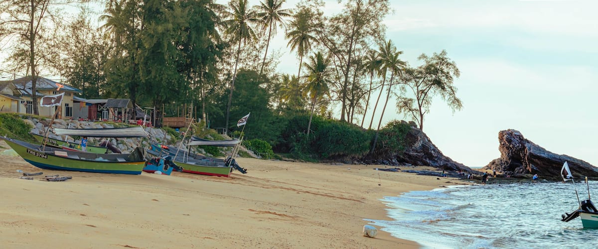 A beach with boats, a rocky outcrop, and a building with a flag.