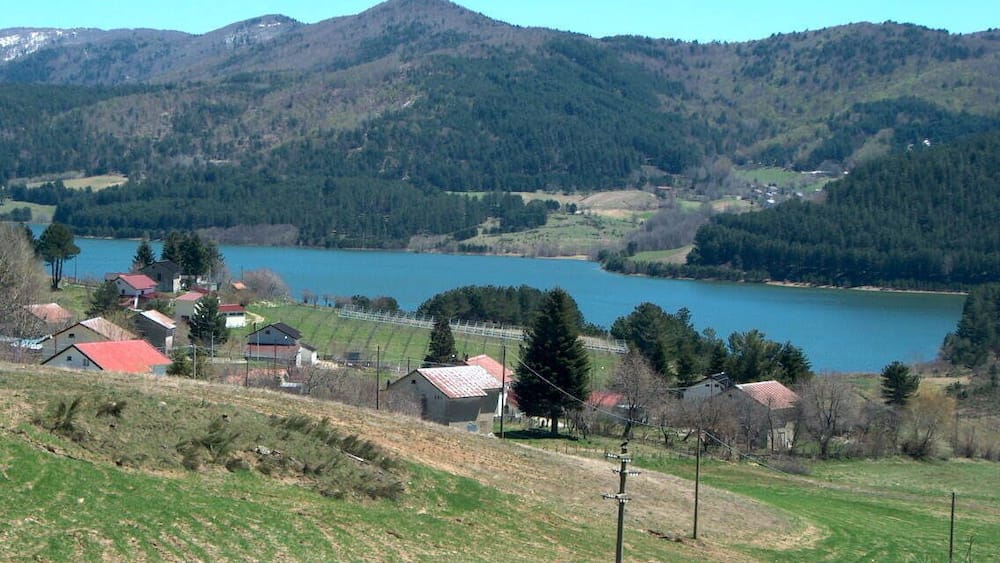 A lake surrounded by hills, houses, and a clear sky.