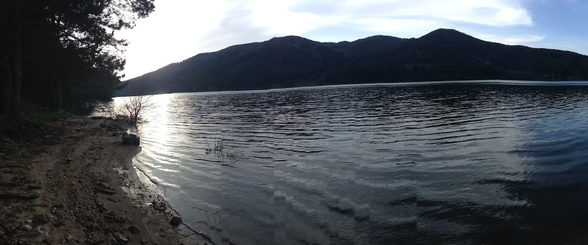 A calm lake with mountains in the background and trees framing the scene.