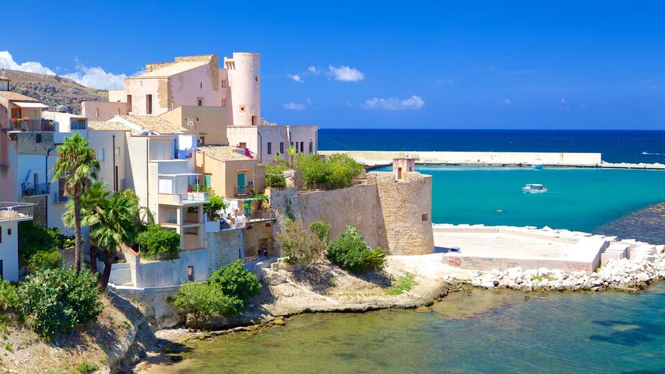 A coastal town with historic buildings, a clear blue sea, and a rocky shoreline.