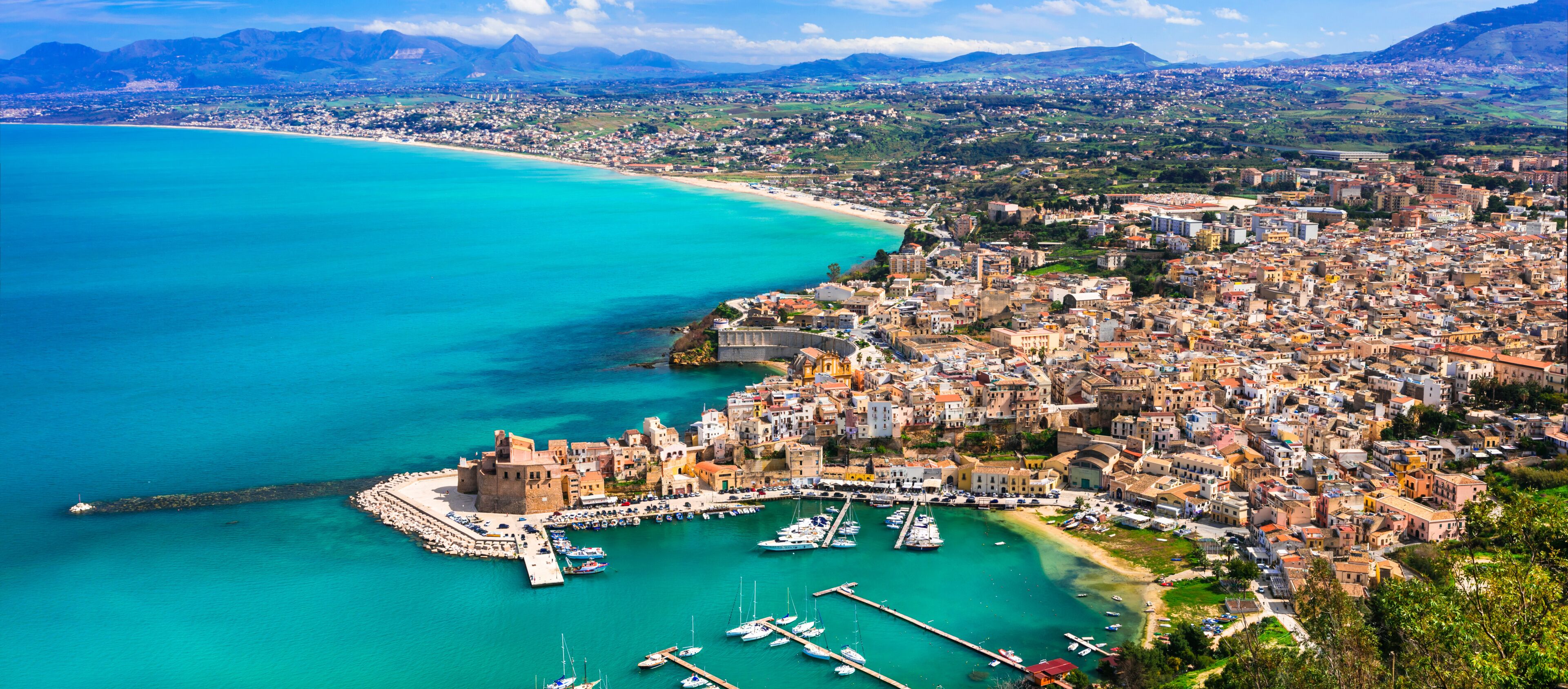 A coastal city with a historic fort, a marina, and a mountainous backdrop.