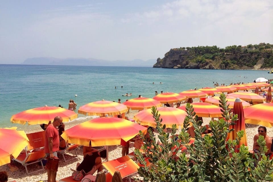 Una platja amb nombrosos para-sols i gent banyant-se.