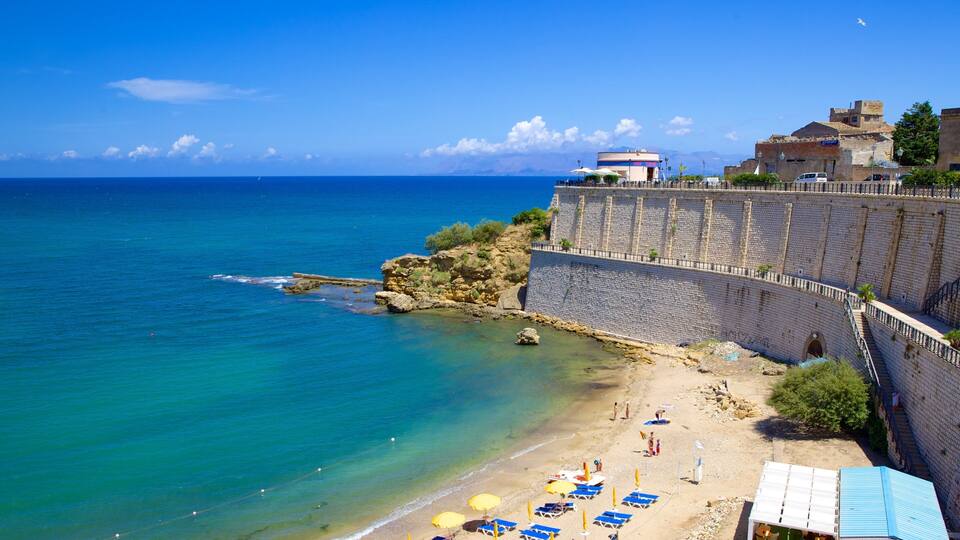 A coastal town with a beach, clear blue sea, and a stone wall.