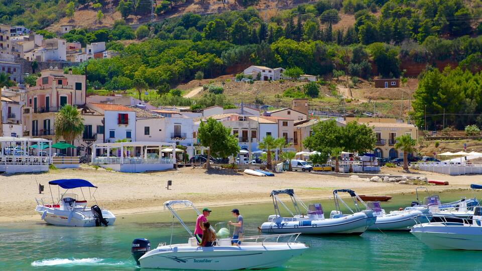 A coastal village with boats docked along the shore, a sandy beach, and buildings with red-tiled roofs.