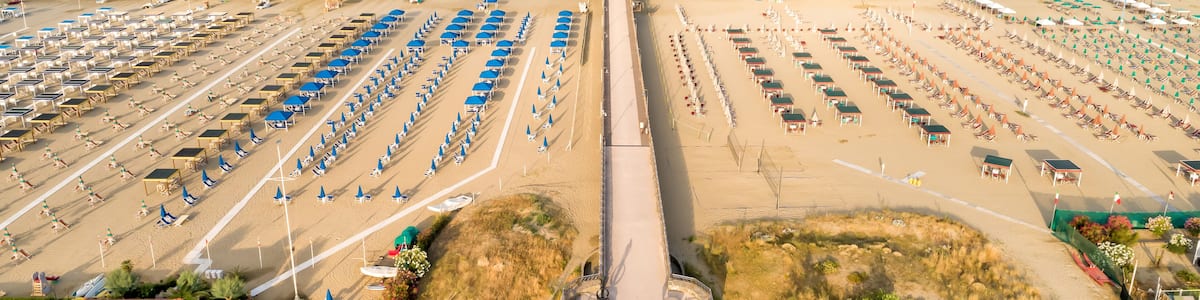 Une plage bordée de rangées de parasols et de chaises longues, une jetée qui s’avance dans l’eau et un ciel dégagé.