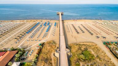 A beach with rows of umbrellas and lounge chairs, a pier extending into the water, and a clear sky.