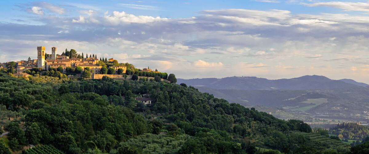 A historic town with a prominent tower, lush green hills, and distant mountains.