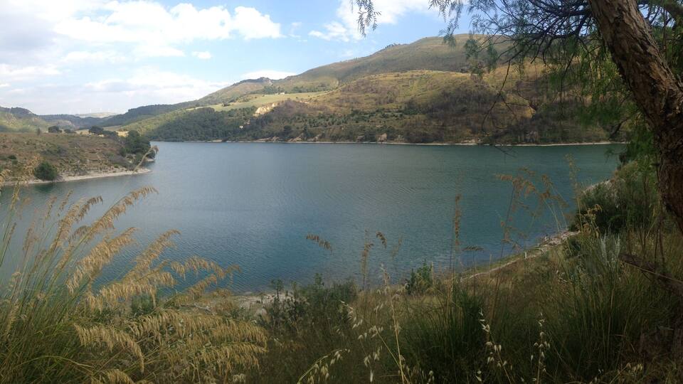 A lake surrounded by hills with wind turbines in the distance.