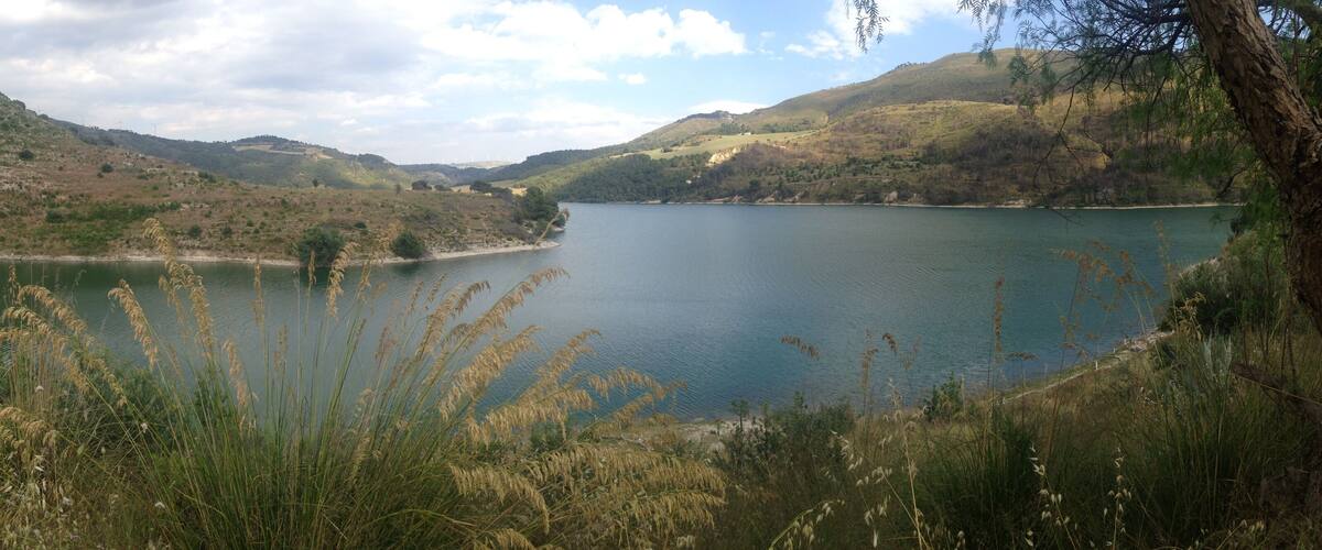 A lake surrounded by hills with wind turbines in the distance.