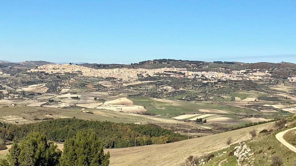 A panoramic view of a town nestled in a valley with rolling hills and scattered fields.