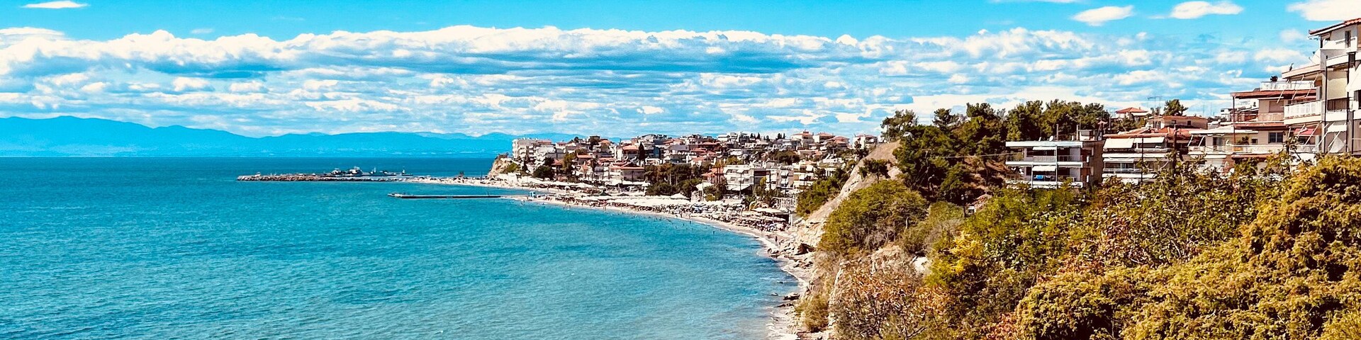 A coastal town with a clear blue sea, a sandy beach, and buildings along the coastline.