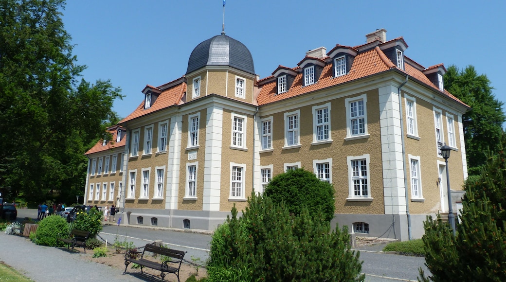 A large, historic building with a dome and red-tiled roof, surrounded by greenery and a paved walkway.