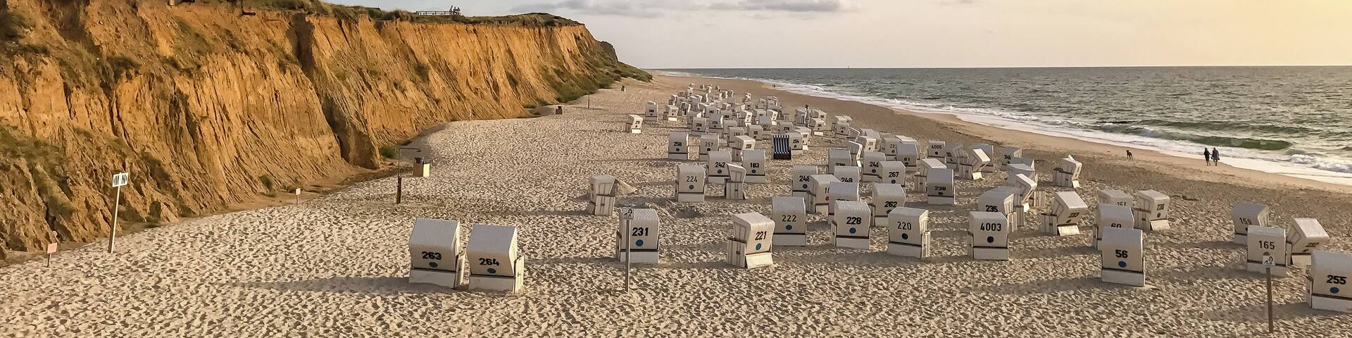 A beach with numbered beach huts and cliffs in the background.