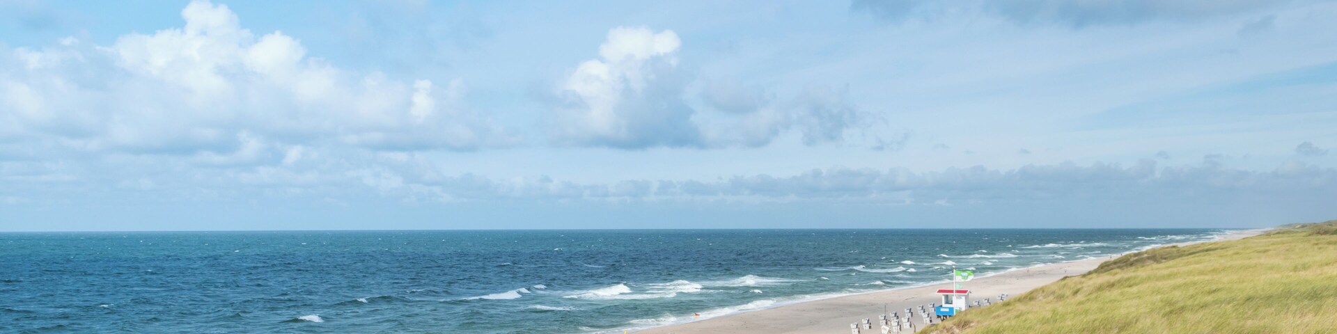 A beach with rows of beach chairs and a lifeguard tower.