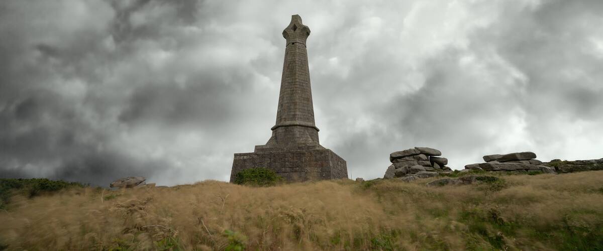 A tall stone monument on a grassy hill with a cloudy sky in the background.