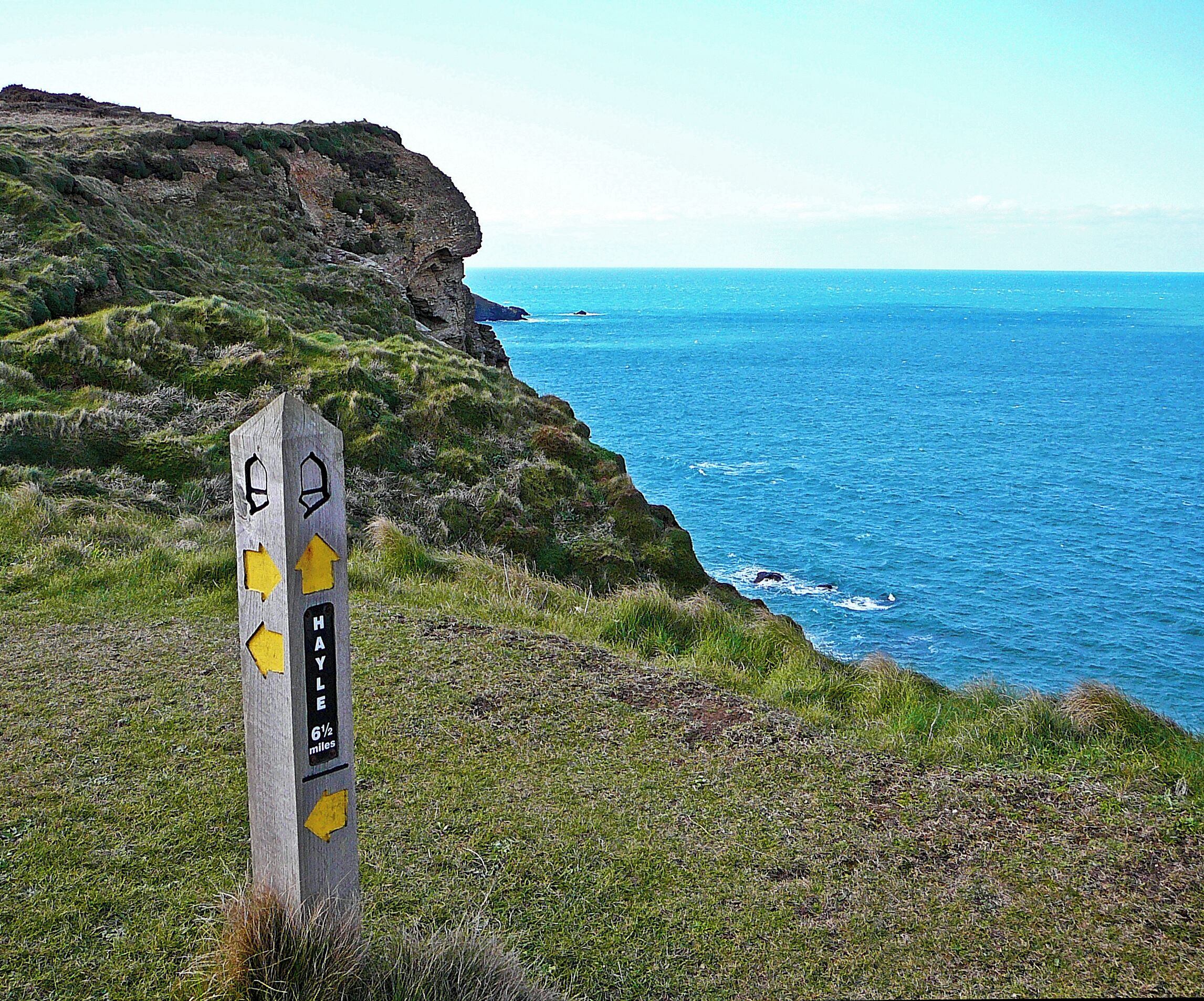 A coastal landscape with a wooden signpost indicating a 6½-mile trail.