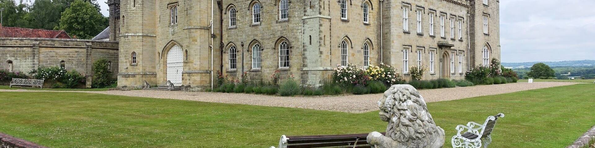A historic castle with a well-maintained lawn, a statue of a lion, and a bench.
