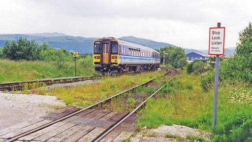 Foxfield: train leaving for Whitehaven, 1998. View northwards, up Dunnerdale towards Coniston ahead - to which the now vanished ex-Furness Railway branch used to go until 6/4/62, the passenger service having ceased since 6/10/58. The Class 153 DMU, on a Carnforth - Barrow-in-Furness - Whitehaven service on the ex-Furness Railway main line, will very soon curve left to cross the Duddon Viaduct, then go south to Millom before continuing up the coast to Whitehaven. Note the weed-strewn tracks. In the distance are Thwaites Fell (1,001 ft.), Burn Moor (1,780 ft.) and Whitwell (1,861 ft.).