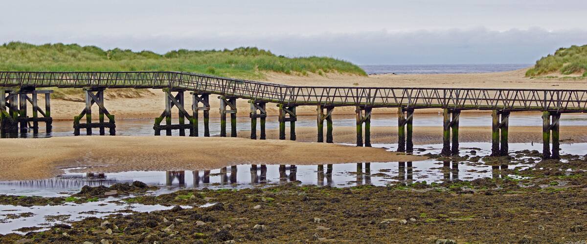 A wooden pier extending over a sandy beach with water at its base.
