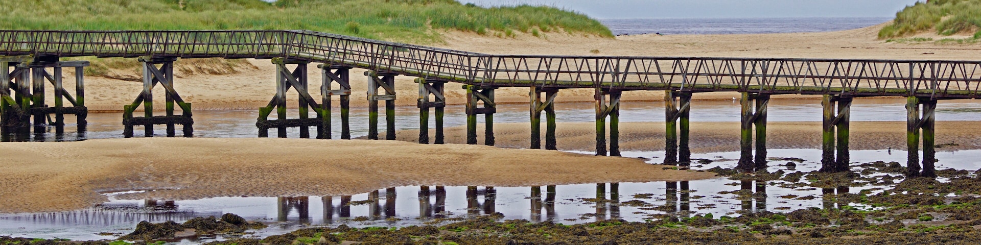 A wooden pier extending over a sandy beach with water at its base.
