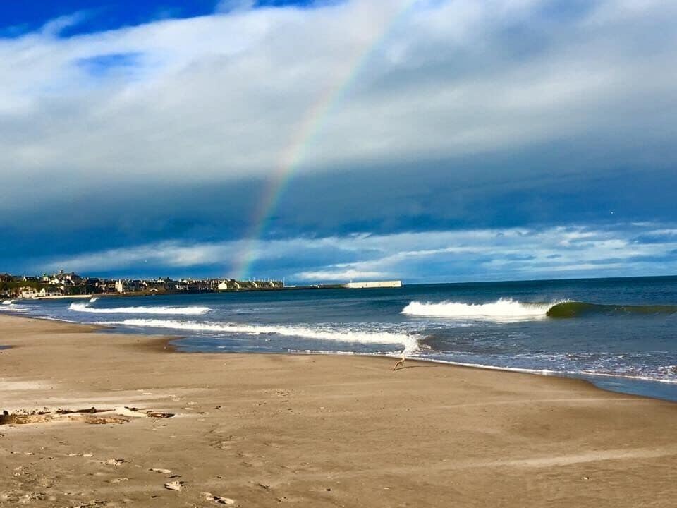 A beach with waves, a rainbow, and a distant pier.