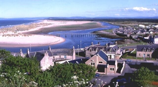 A coastal town with a sandy beach, a pier, and residential buildings.
