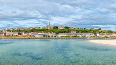 A coastal town with a prominent church on a hill, a sandy beach, and calm waters.