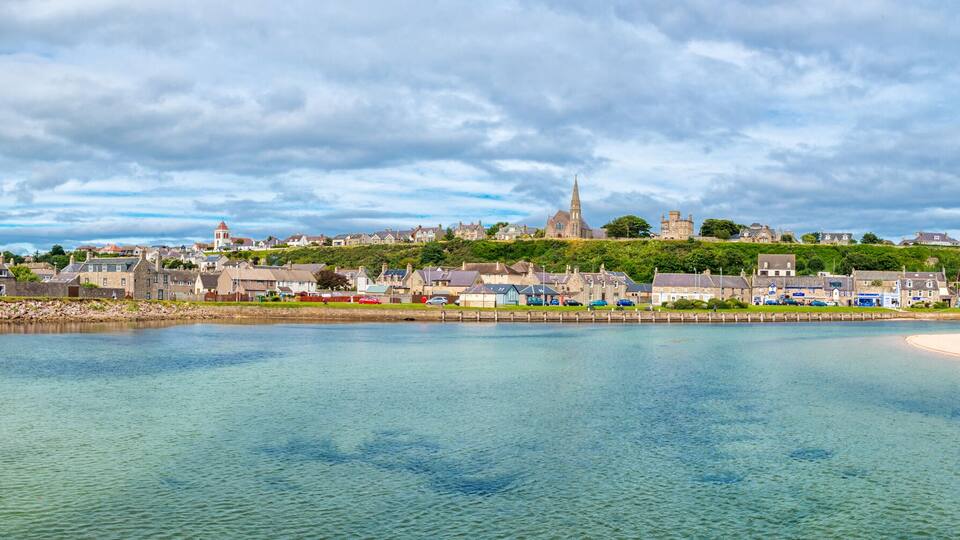 A coastal town with a prominent church on a hill, a sandy beach, and calm waters.